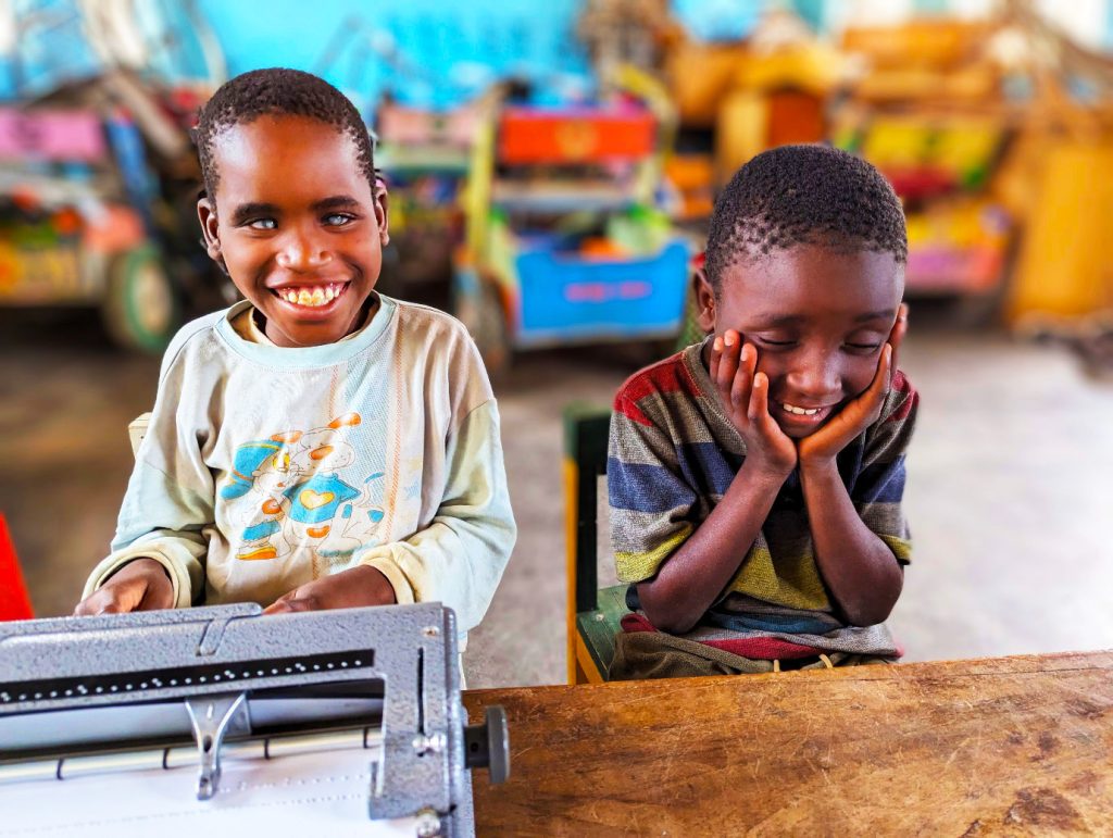 Esther and Layton, 2 children who are visually impaired, share a joke whilst learning how to operate the braille machine.