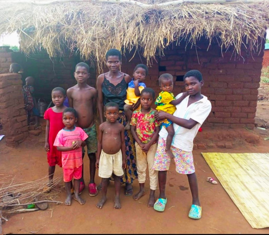 Simon standing with his family of 7 siblings and mum in front of their rural house.